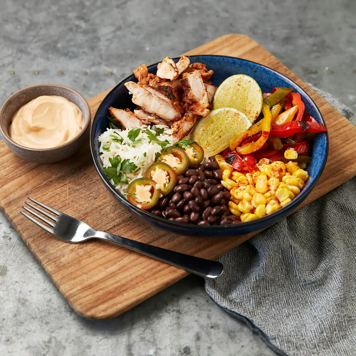 A chicken burrito bowl with rice, black beans, corn, peppers and lime